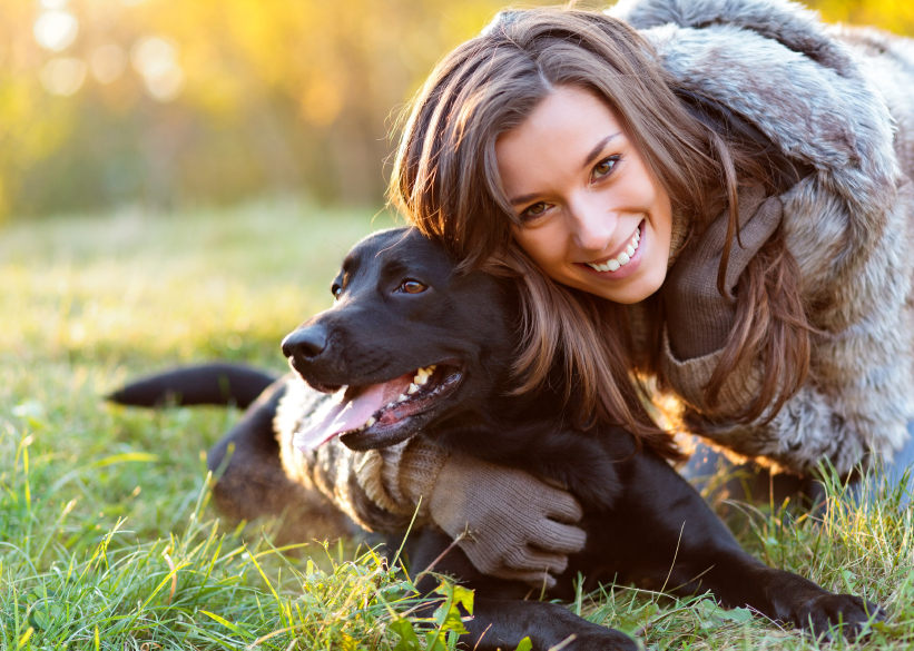 woman-with-dog-black-labrador-smiling-grass-sunshine